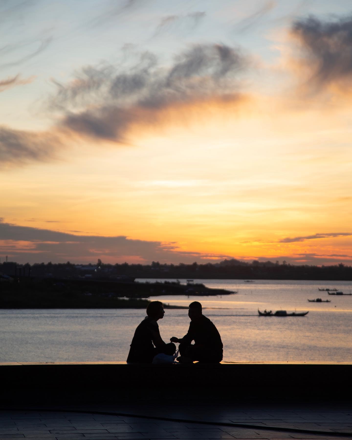 Two people in conversation beside the river at sunset