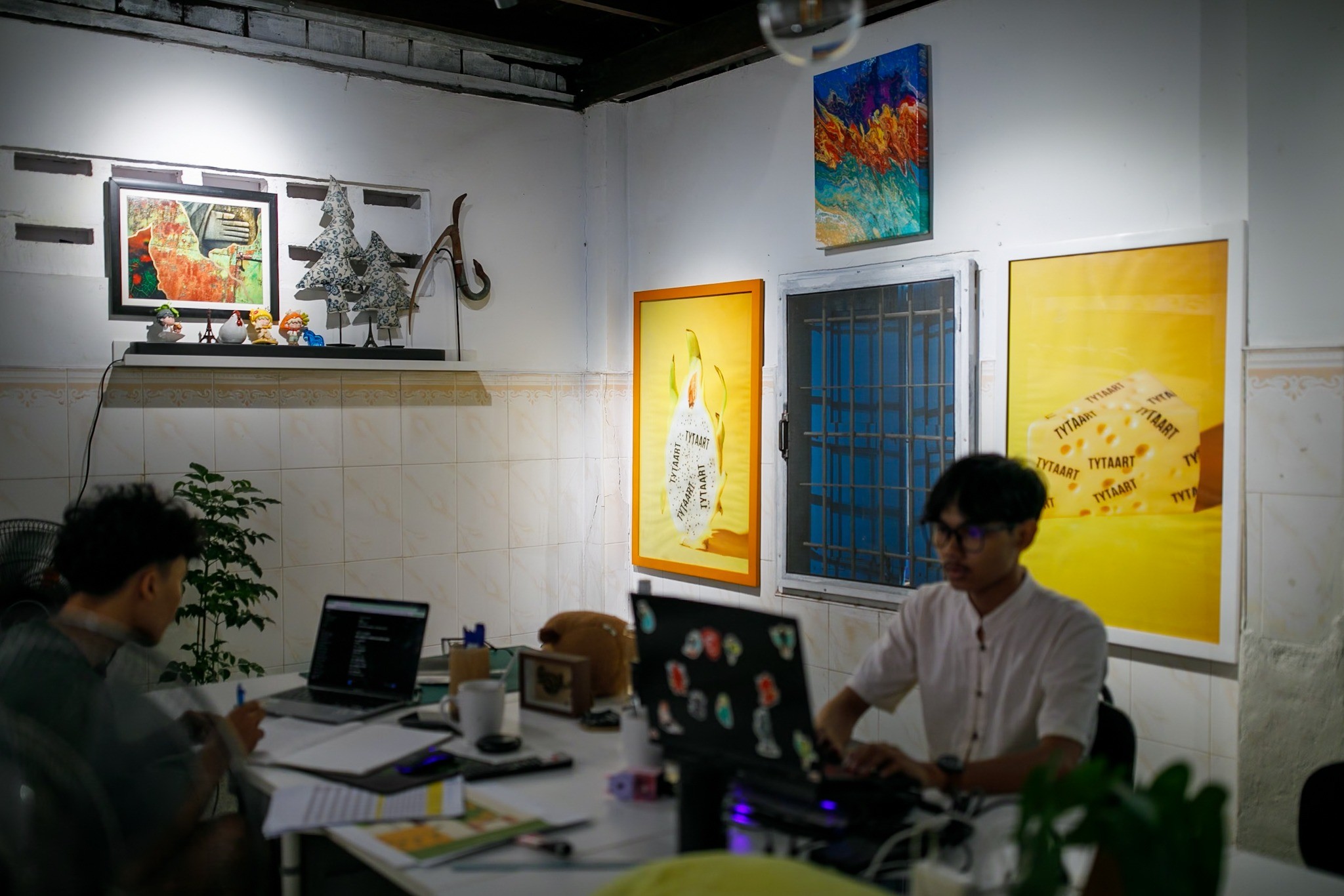 Two team members working on laptops in a room with artworks